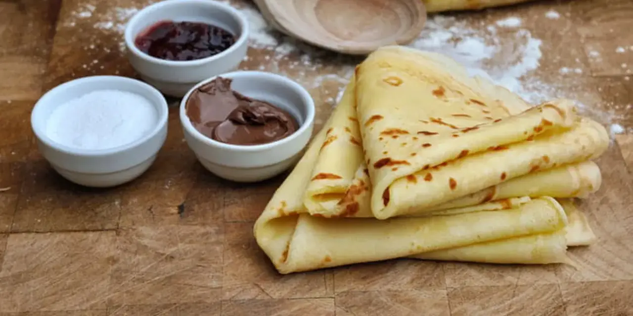 Crêpes dorées empilées, accompagnées de confiture, de pâte à tartiner au chocolat et de sucre. Un délice pour le petit-déjeuner ou le goûter.