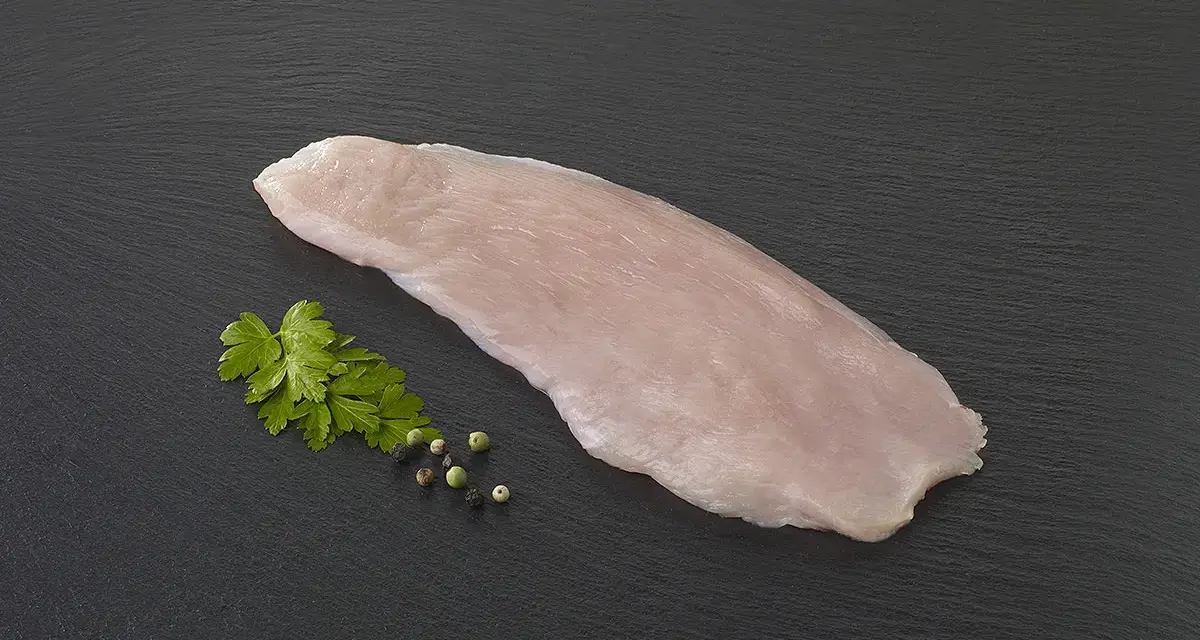 Une escalope de dinde crue, prête à être cuisinée, accompagnée de persil frais et de grains de poivre sur fond sombre.