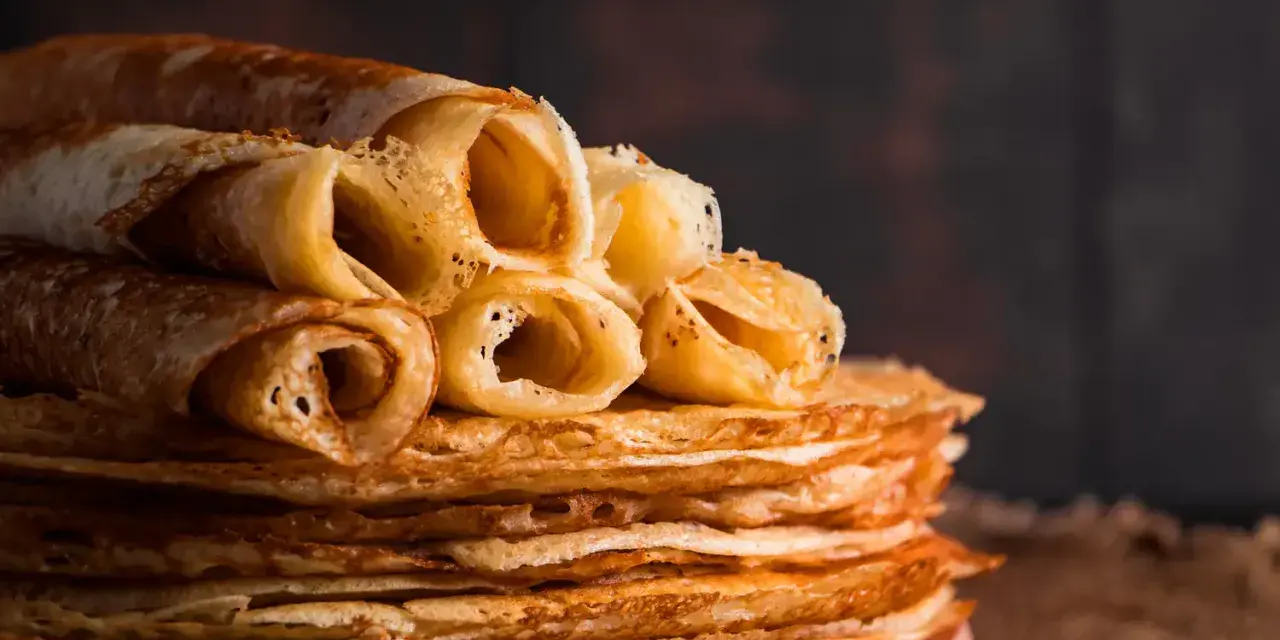 Pile de crêpes dorées, certaines roulées, prêtes à être dégustées. Une astuce pour garder les crêpes au chaud : les empiler ainsi !