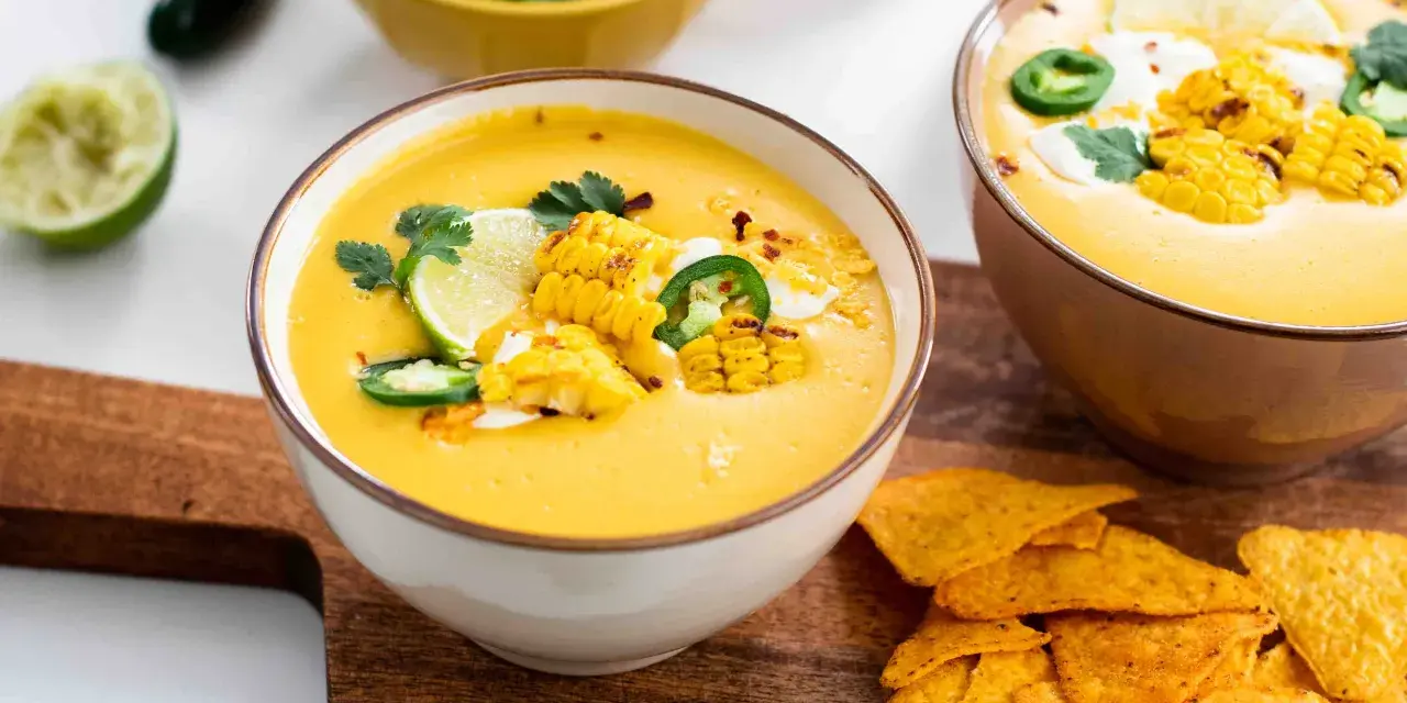 Soupe de légumes crémeuse, garnie de maïs grillé, jalapeños, coriandre et quartiers de citron vert. Servie avec des nachos croustillants.