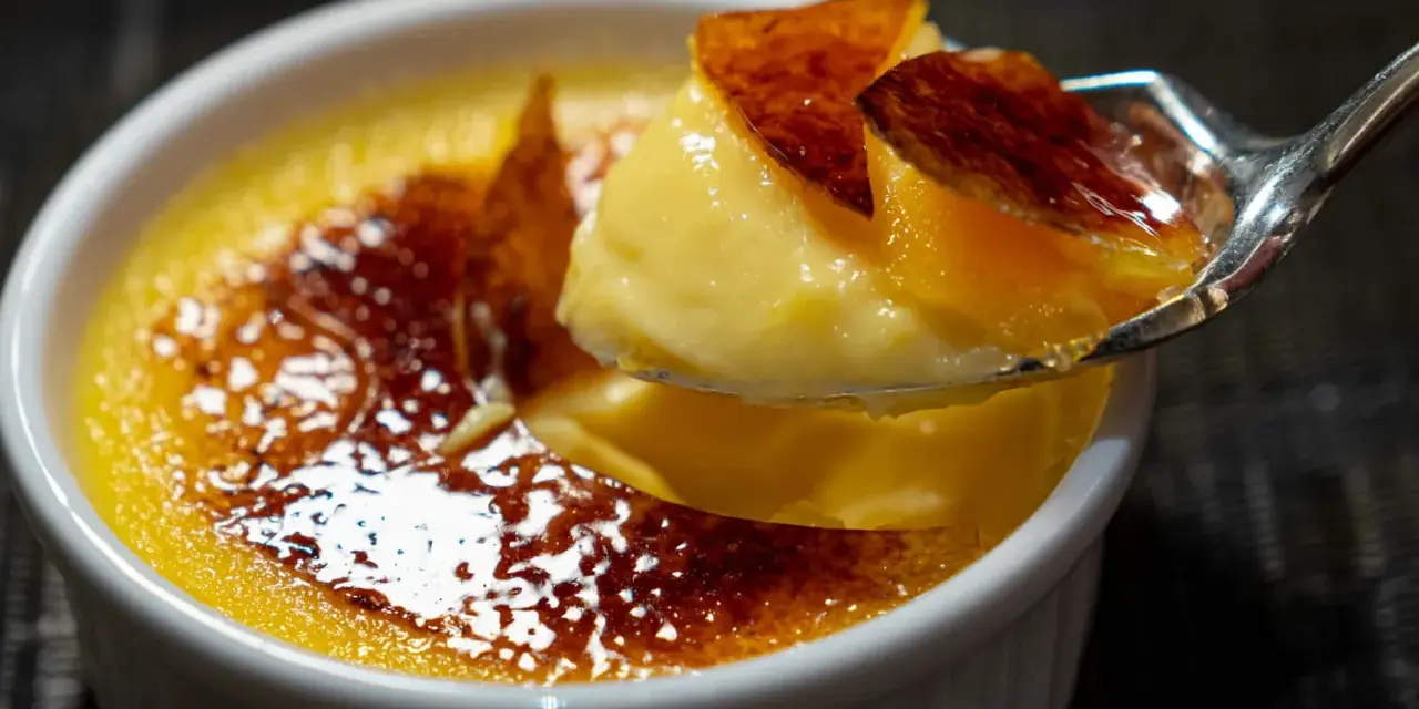 Une cuillère prélève un morceau de crème brûlée, révélant sa texture onctueuse sous une croûte de caramel craquante.
