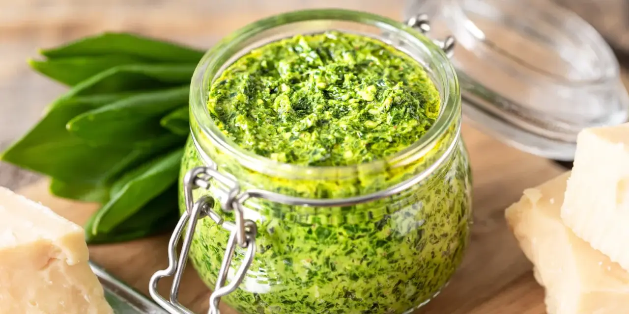Pesto d'ail des ours dans un bocal, avec des feuilles fraîches, du parmesan et des noix. Une recette maison facile à réaliser.