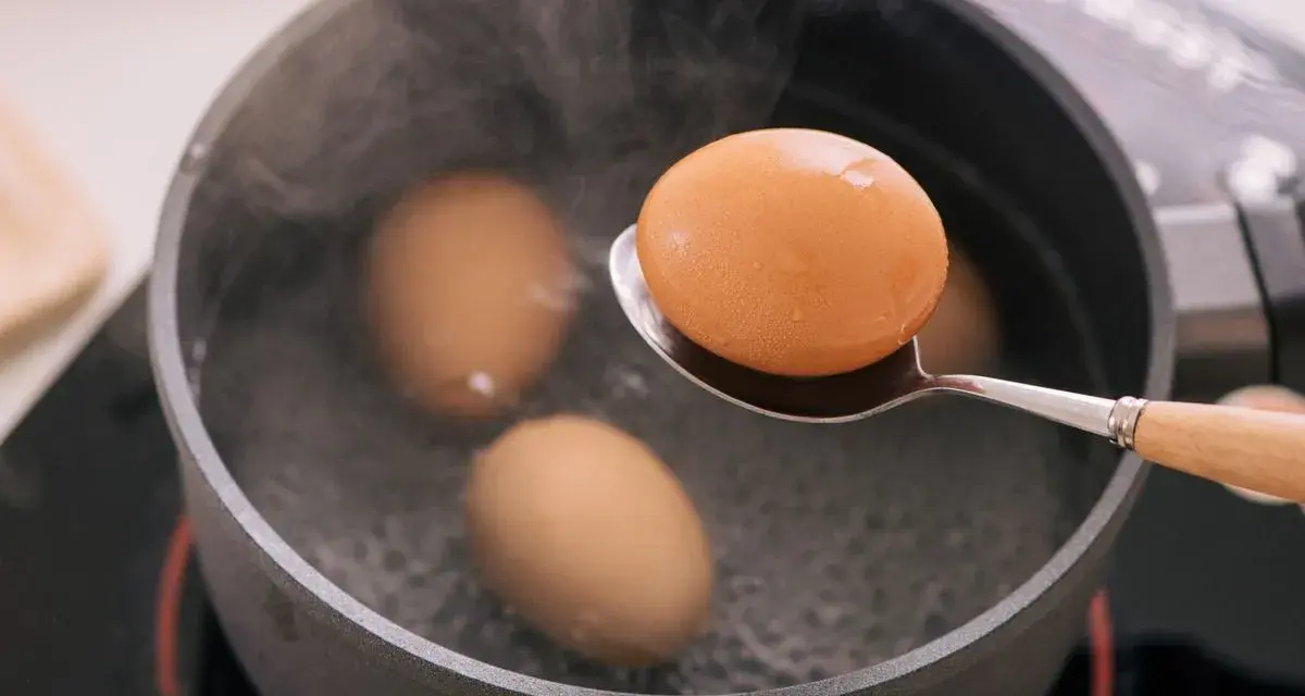 Un œuf mollet est retiré d'une casserole d'eau bouillante à l'aide d'une cuillère. La vapeur s'élève des œufs dans la casserole.