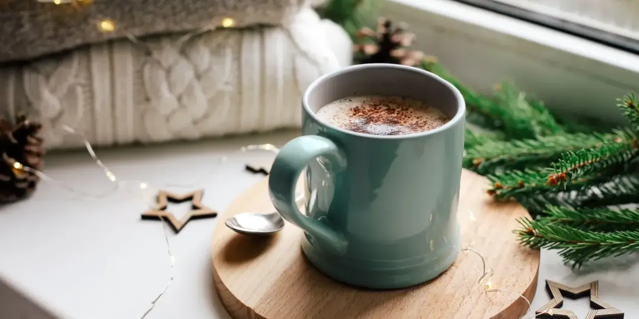 Une tasse de chocolat chaud fumant, entourée de décorations de Noël et de lumières scintillantes, promet un moment de réconfort.