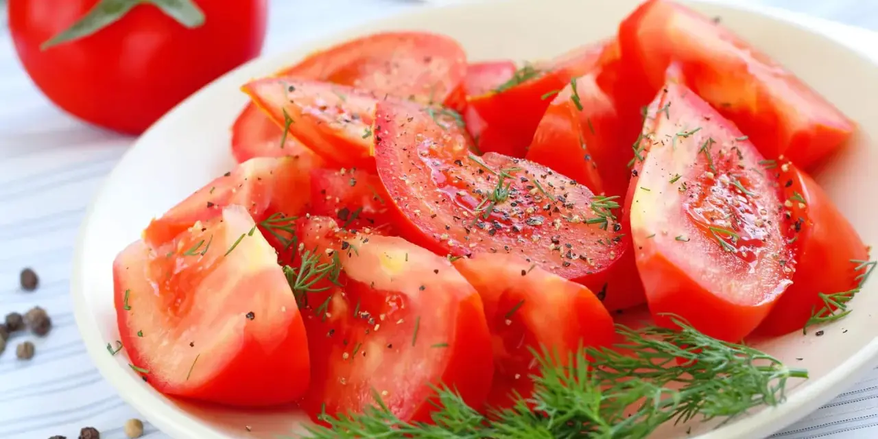 Une assiette de salade de tomates fraîches, assaisonnée de poivre noir et d'aneth. Un délice simple et coloré.