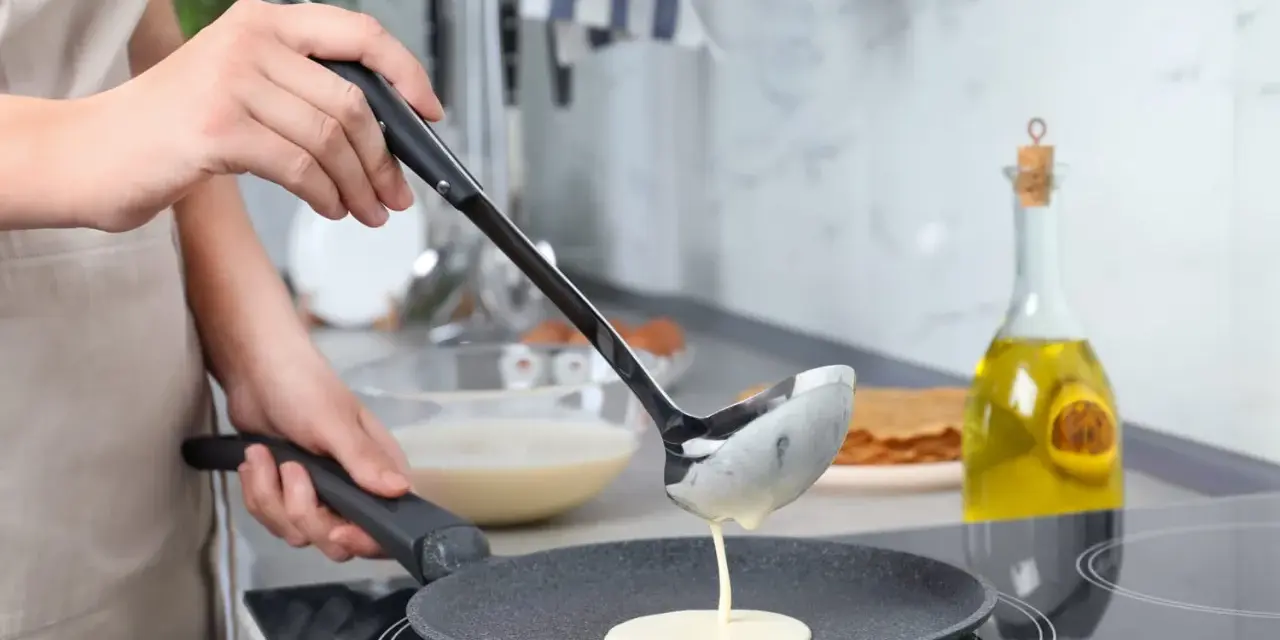 Une louche verse de la pâte à crêpes dans une poêle. On dirait qu'il y a trop de beurre dans la pâte à crêpes, elle est très liquide !
