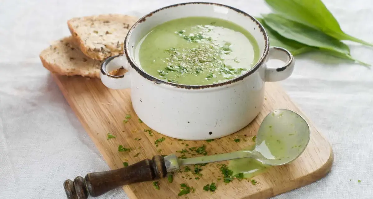 Délicieuse soupe courgette verte, garnie d'herbes fraîches, servie avec du pain grillé et une louche.
