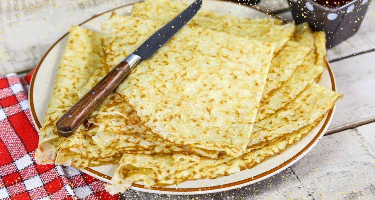 Pile de crêpes bretonnes dorées sur une assiette, prêtes à être dégustées. Un couteau est posé dessus.