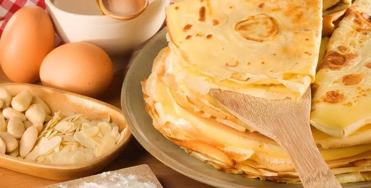 Pile de crêpes dorées, ingrédients pour leur origine : œufs, amandes, farine, miel. Un délice sucré.