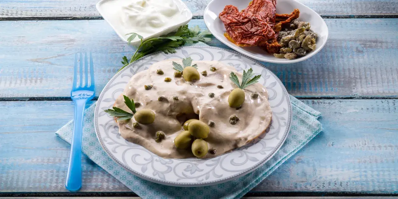 Tête de veau en sauce crémeuse, garnie d'olives et de câpres, accompagnée de tomates séchées et de yaourt.