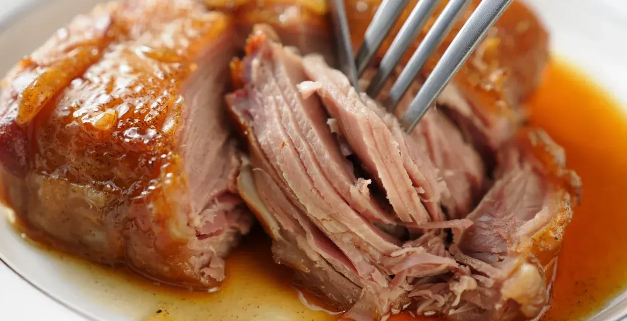 Une rouelle de porc au four, tendre et juteuse, est effilochée à la fourchette dans son jus doré.