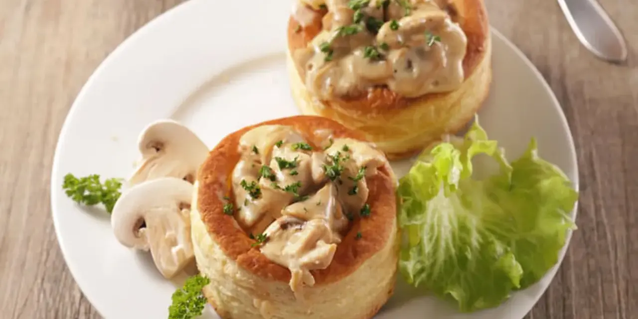Deux bouchées à la reine garnies d'une sauce crémeuse aux champignons, accompagnées de champignons frais et d'une feuille de laitue.