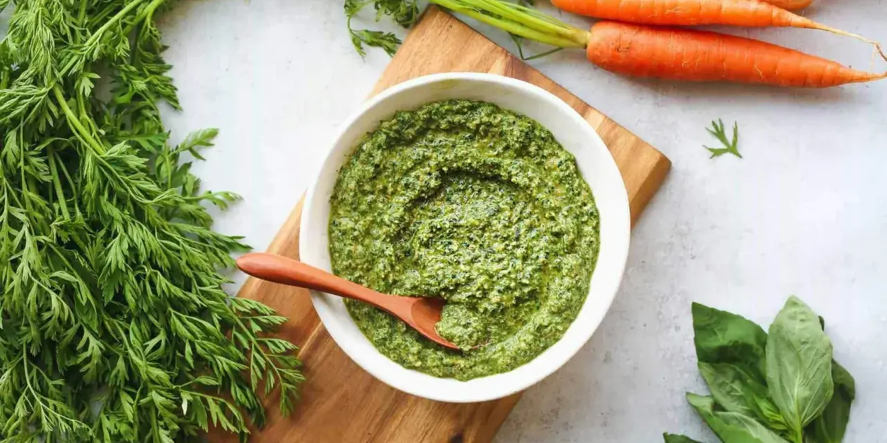 Un bol de pesto de fanes de carottes, avec des carottes fraîches et du basilic à côté.