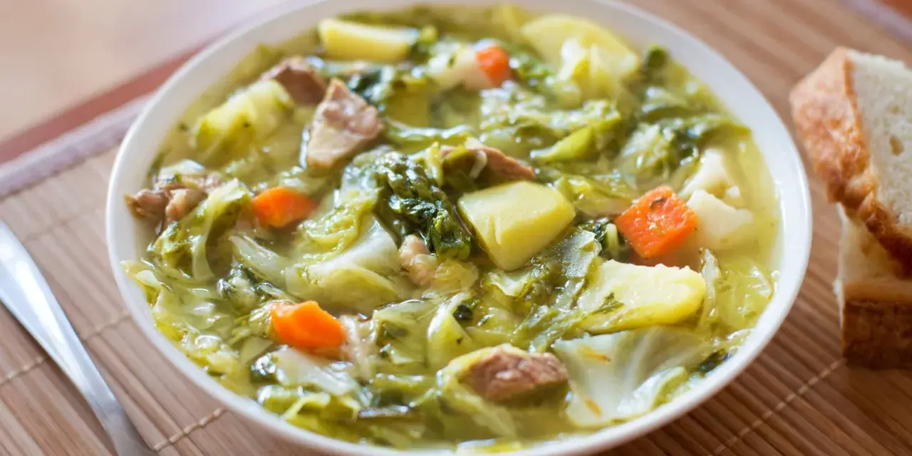 Un bol de soupe aux choux réconfortante, avec des morceaux de chou, pommes de terre, carottes et viande. Du pain frais à côté.