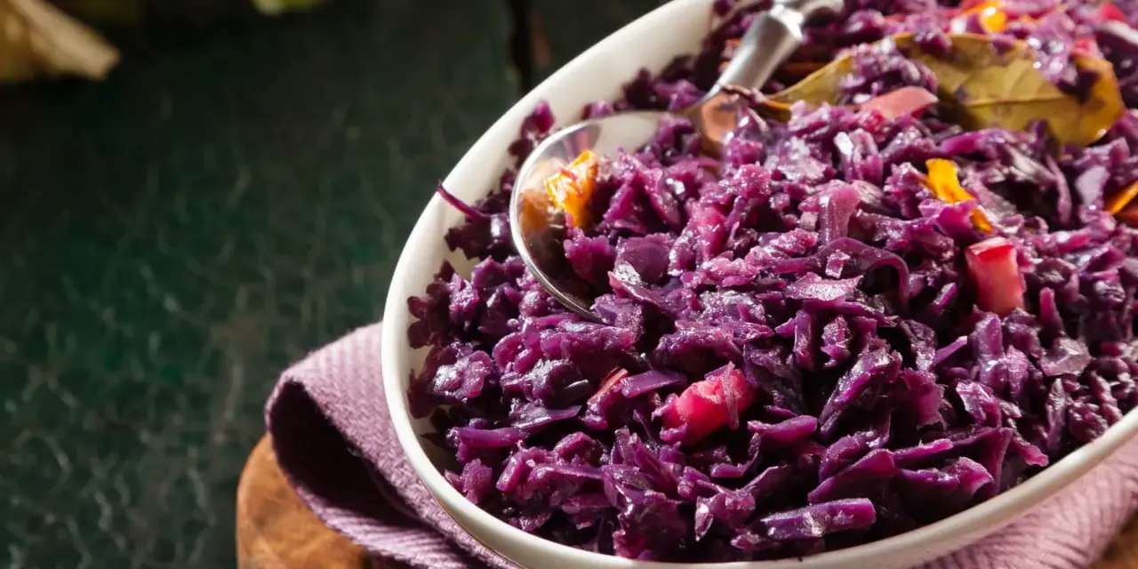 Un plat de chou rouge recette, cuisiné avec des épices et des morceaux de pomme, servi dans un bol blanc.