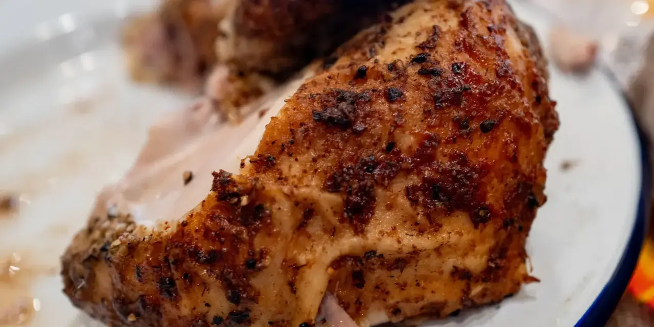 Un morceau de poulet braisé, doré et savoureux, est servi sur une assiette blanche.