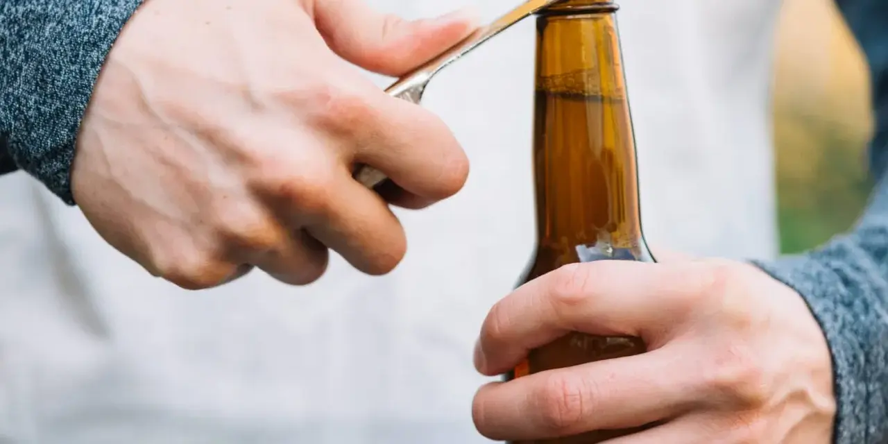 Main gauche tenant une bouteille, main droite utilisant un objet pour ouvrir la bouteille sans tire bouchon.