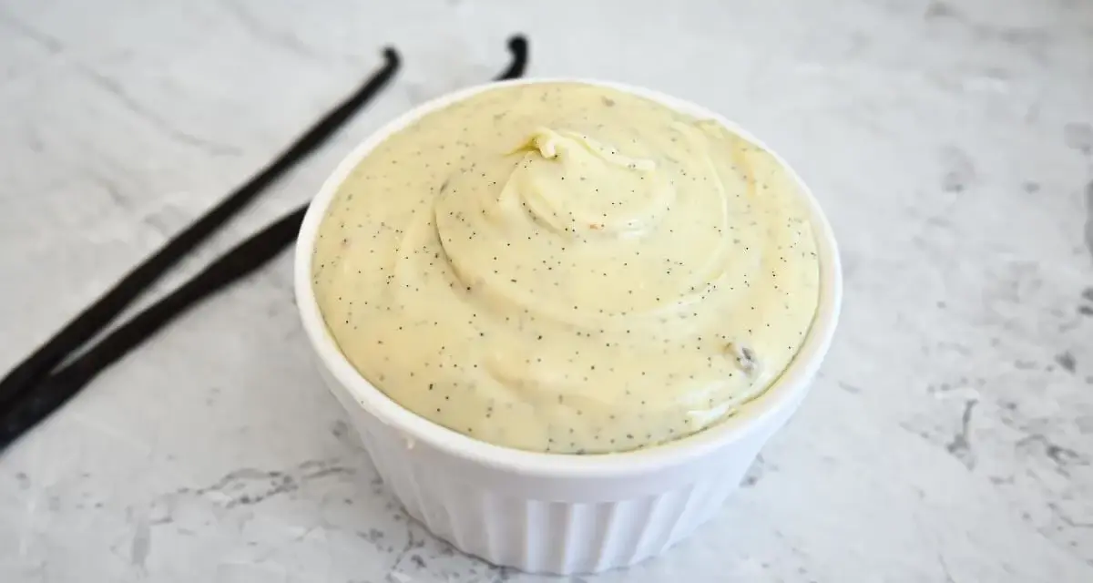 Un bol de ganache chocolat blanc onctueuse, parsemée de points de vanille, avec deux gousses de vanille à côté.