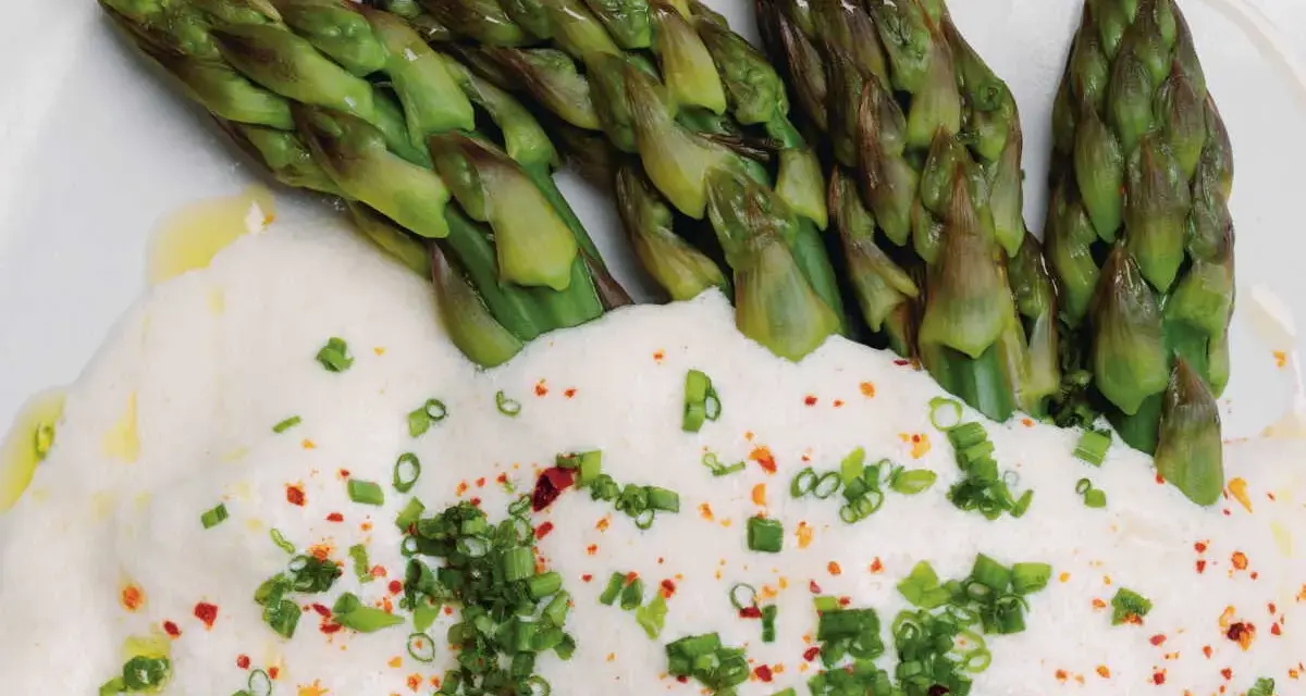 Asperges vertes tendres nappées d'une onctueuse sauce mousseline, parsemées de ciboule et de piment. Un délice printanier.