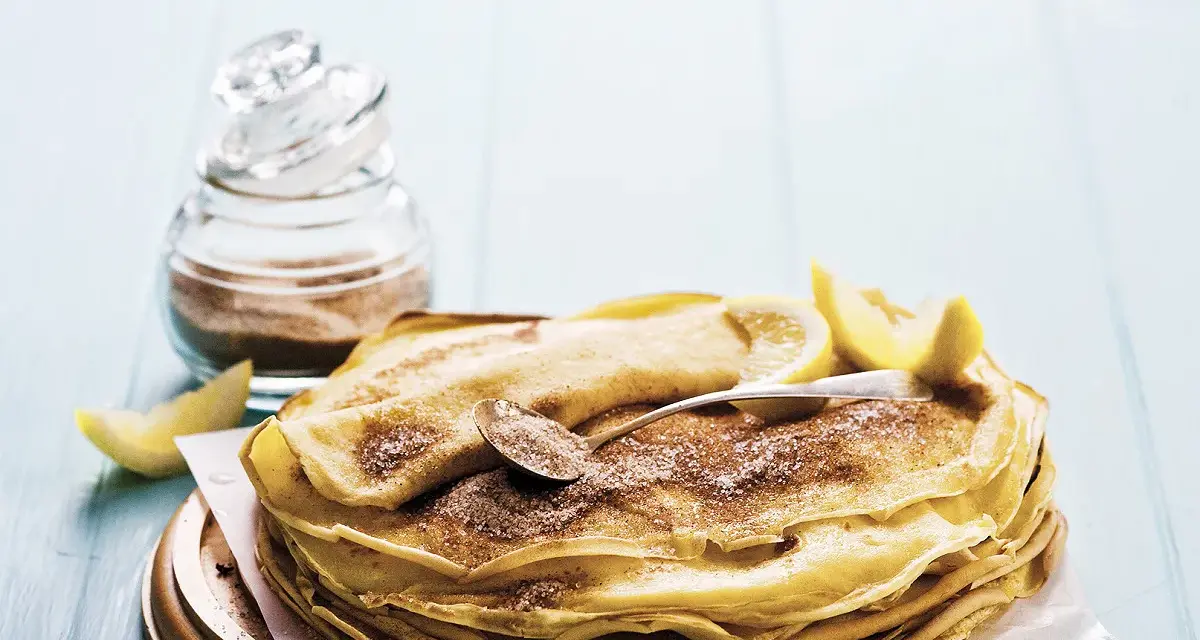 Pile de crêpes au lait entier, saupoudrées de sucre et de cannelle, garnies de quartiers de citron. Un délice simple et gourmand.
