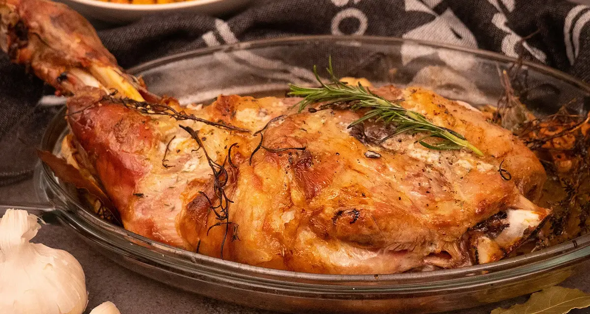 Une succulente épaule d'agneau rôtie à la perfection, garnie de romarin frais, prête à être dégustée.
