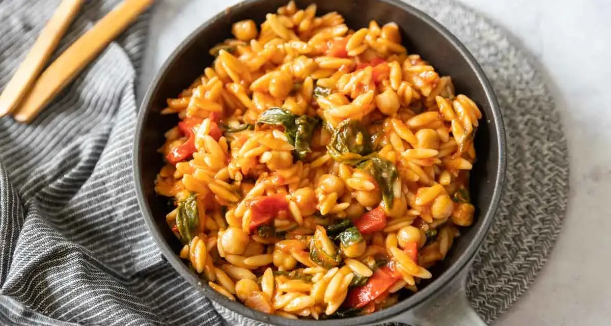 Un plat de cuisson orzo savoureux avec des pois chiches, des poivrons rouges et des épinards dans une sauce tomate.