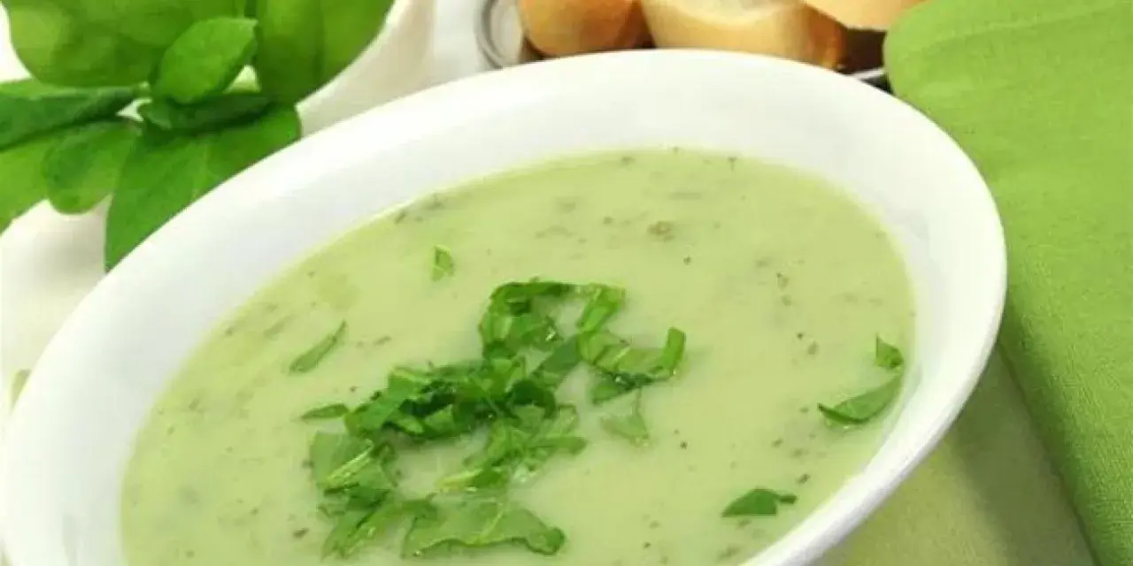 Un bol de soupe à l'oseille crémeuse, garnie d'herbes fraîches, avec du pain en arrière-plan.