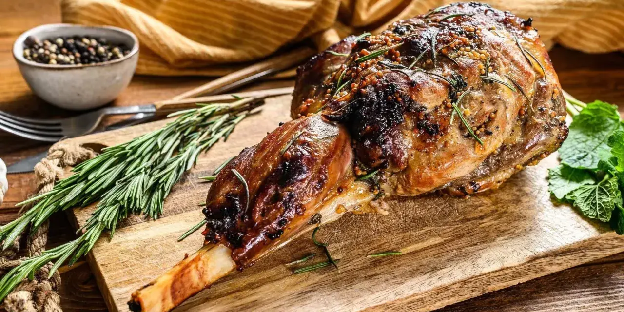 Gigot d'agneau rôti, doré et savoureux, garni de romarin et de moutarde, prêt à être dégusté.