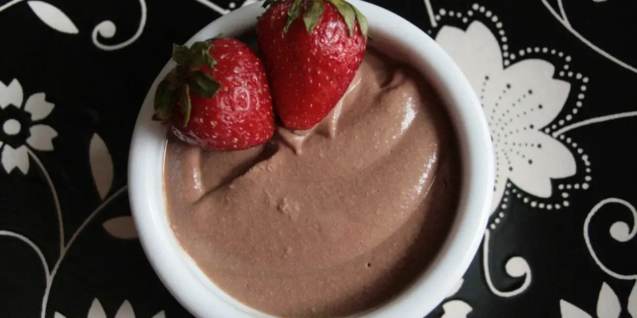 Délicieuse crème au chocolat onctueuse, garnie de deux fraises fraîches, servie dans un bol blanc sur une assiette noire décorée.