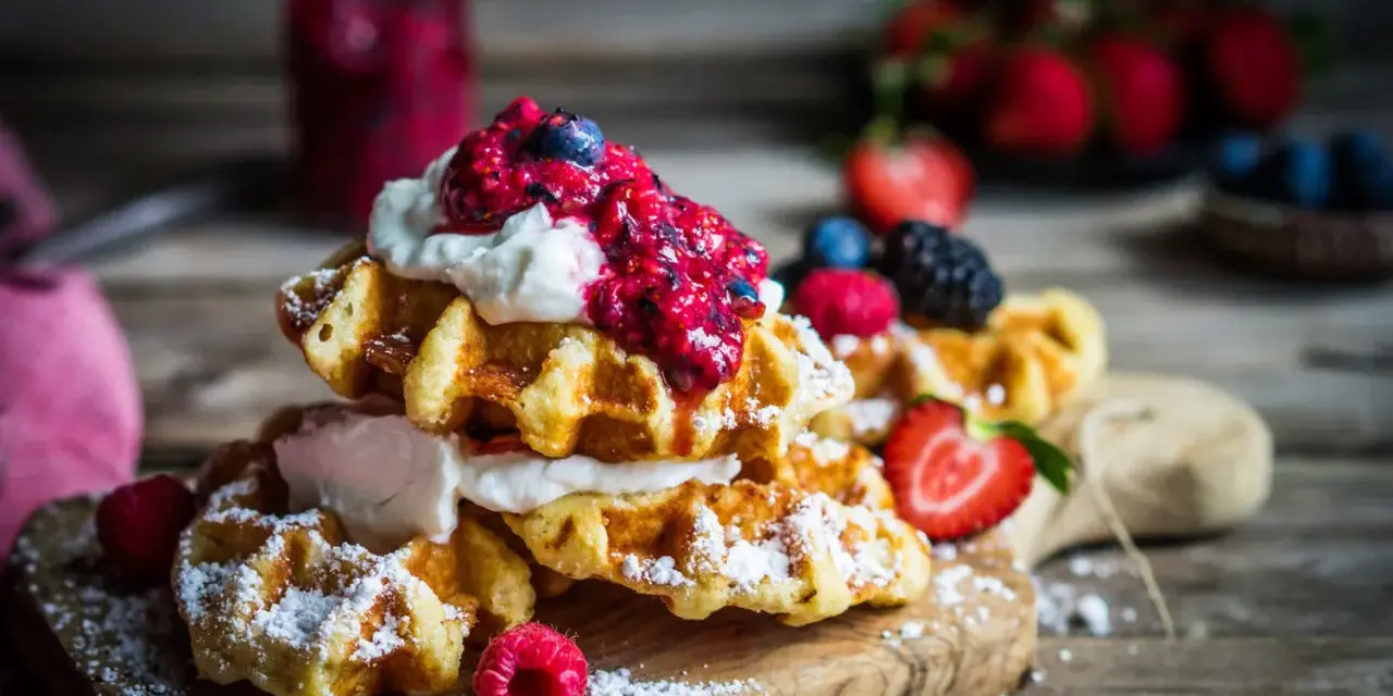Pile de gaufres traditionnelles garnies de crème fouettée et de fruits rouges, saupoudrées de sucre glace. Un délice pour une recette de gaufre traditionnelle réussie.