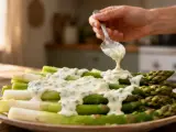 Une main verse une sauce légère pour asperges sur un plat d'asperges vertes et blanches.