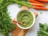 Un bol de pesto de fanes de carottes, avec des carottes fraîches et du basilic à côté.