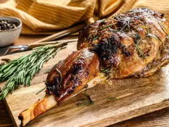 Gigot d'agneau rôti, doré et savoureux, garni de romarin et de moutarde, prêt à être dégusté.