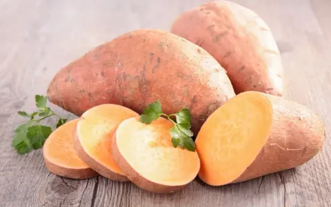 Patates douces entières et tranchées, prêtes à cuire. Une touche de persil frais pour la décoration.