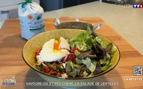 Une assiette colorée de salade de lentilles garnie d'un œuf poché, de légumes frais et de tomates. Un sac de lentilles vertes est visible en arrière-plan.