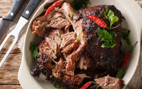 Gigot d'agneau au four cuisson lente, effiloché, garni de piments rouges et de persil frais. Un délice à partager.