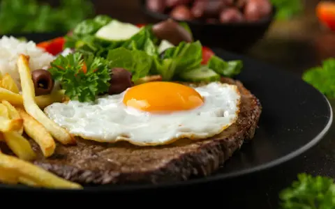 Un plat de steak a cheval savoureux avec un œuf au plat, des frites dorées, du riz blanc et une salade fraîche.