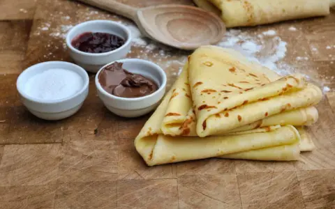 Crêpes dorées empilées, accompagnées de confiture, de pâte à tartiner au chocolat et de sucre. Un délice pour le petit-déjeuner ou le goûter.