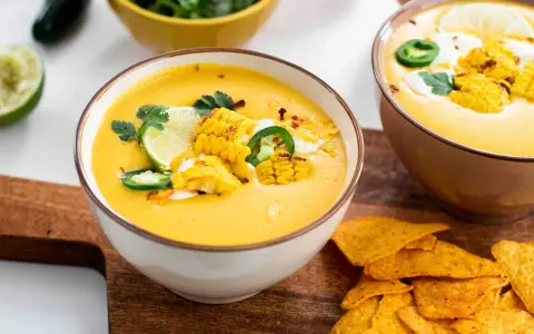 Soupe de légumes crémeuse, garnie de maïs grillé, jalapeños, coriandre et quartiers de citron vert. Servie avec des nachos croustillants.