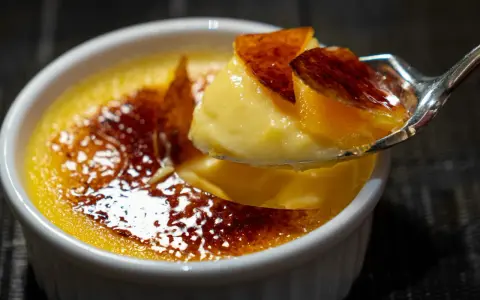 Une cuillère prélève un morceau de crème brûlée, révélant sa texture onctueuse sous une croûte de caramel craquante.