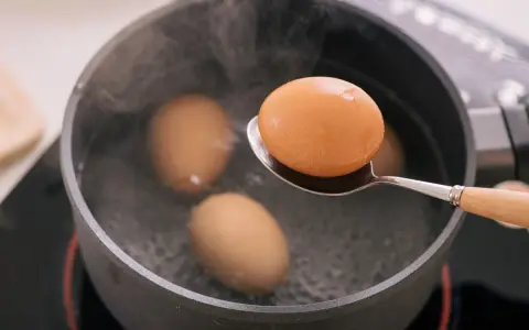 Un œuf mollet est retiré d'une casserole d'eau bouillante à l'aide d'une cuillère. La vapeur s'élève des œufs dans la casserole.