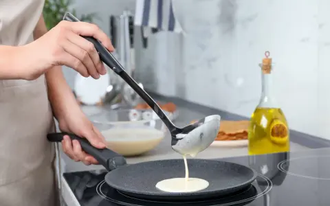 Une louche verse de la pâte à crêpes dans une poêle. On dirait qu'il y a trop de beurre dans la pâte à crêpes, elle est très liquide !