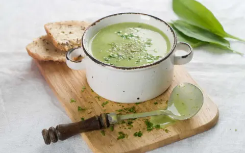 Délicieuse soupe courgette verte, garnie d'herbes fraîches, servie avec du pain grillé et une louche.
