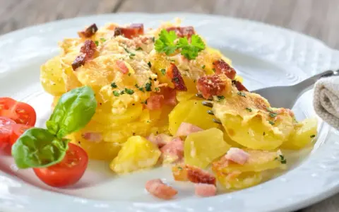 Un délicieux gratin de pommes de terre et lardons, doré au four, servi avec des tomates cerises et du basilic. Un plat réconfortant et savoureux.