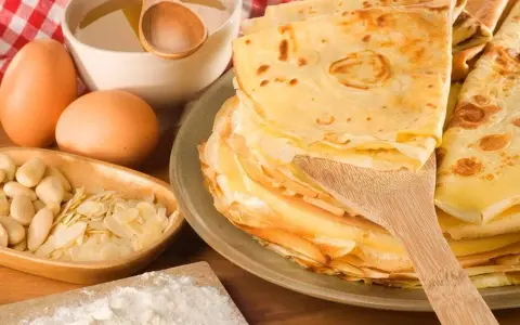 Pile de crêpes dorées, ingrédients pour leur origine : œufs, amandes, farine, miel. Un délice sucré.