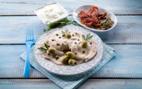 Tête de veau en sauce crémeuse, garnie d'olives et de câpres, accompagnée de tomates séchées et de yaourt.
