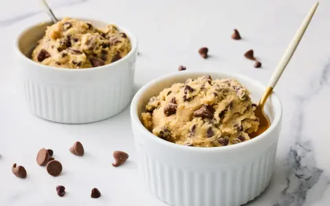 Deux ramequins blancs remplis de pâte à cookie aux pépites de chocolat, prêts à être dégustés.