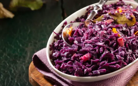 Un plat de chou rouge recette, cuisiné avec des épices et des morceaux de pomme, servi dans un bol blanc.