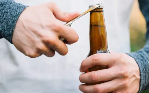 Main gauche tenant une bouteille, main droite utilisant un objet pour ouvrir la bouteille sans tire bouchon.
