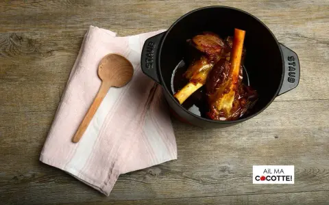 Souris d'agneau à la cocotte en fonte, tendres et savoureuses, prêtes à être dégustées. Une cuillère en bois et une serviette rose complètent la scène.